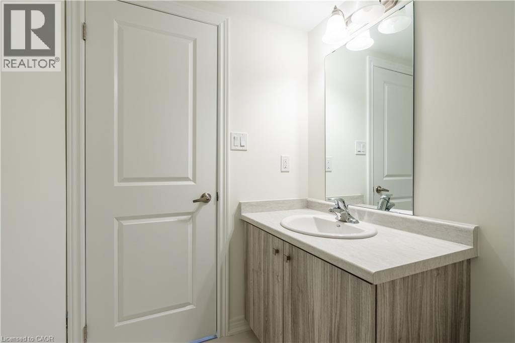 Vanity with wood-finish cabinetry, integrated sink, chrome faucet, and a wall-mounted mirror - 23 Dryden Lane, Hamilton, ON
