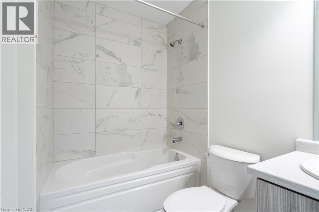 Bathtub with surrounding white and gray veined tile, chrome shower fixtures, and a toilet - 23 Dryden Lane, Hamilton, ON