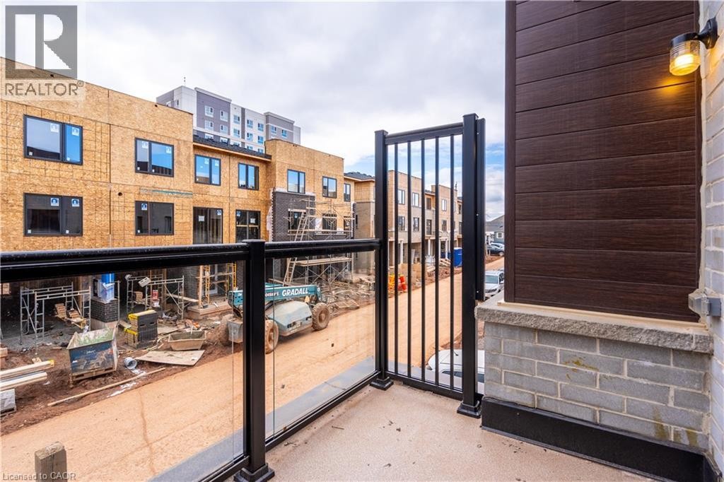 Balcony featuring a glass and metal railing, concrete flooring, dark wood-finish siding, exterior brickwork, and an attached outdoor light fixture - 23 Dryden Lane, Hamilton, ON