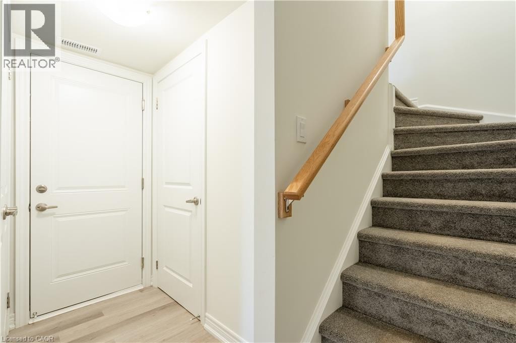 Light wood-finish flooring, two white panel doors with brushed nickel hardware, light gray wall paint, carpeted staircase, and wood handrail - 23 Dryden Lane, Hamilton, ON