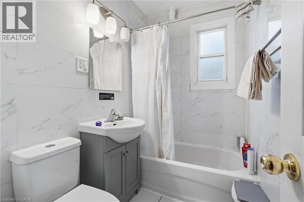 Full bathroom featuring a white tile surround, a built-in bathtub, and a window with frosted glass - 139 Dalewood Avenue, Hamilton, ON
