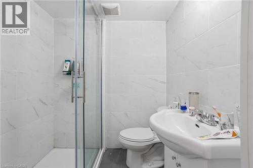 Bathroom featuring a glass-enclosed shower, white ceramic wall tiles with subtle veining, grey wood-finish flooring, a pedestal sink with chrome fixtures, and an exhaust fan - 139 Dalewood Avenue, Hamilton, ON 