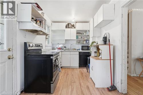 Compact kitchen featuring wood-finish flooring, white cabinetry, a black electric range, and a black dishwasher - 139 Dalewood Avenue, Hamilton, ON 