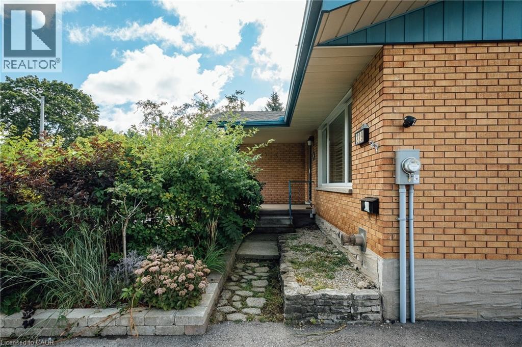 Brick exterior with a peaked roofline, front entry with steps, and established landscaping - 229 Winfield Avenue, Waterloo, ON