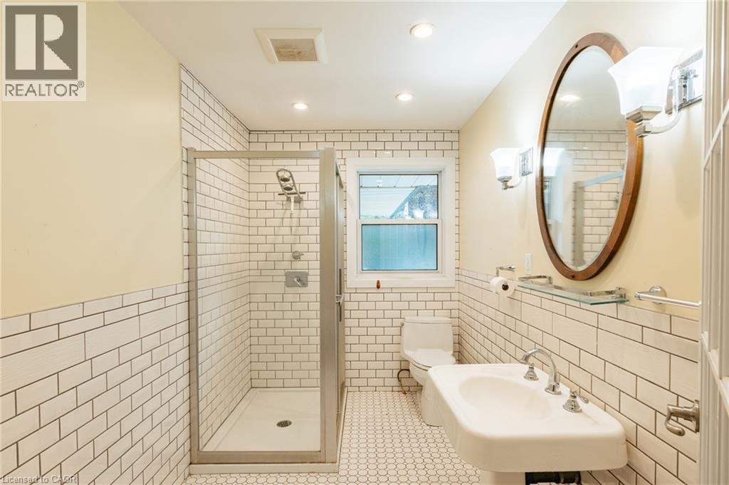 Bathroom featuring subway tile wainscoting, a pedestal sink, a glass-enclosed shower, a framed oval mirror, and recessed lighting - 229 Winfield Avenue, Waterloo, ON