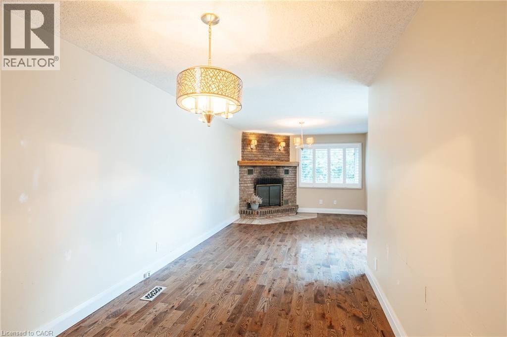 Wood-finish flooring, corner brick fireplace with wood mantel, decorative chandelier, and window with plantation shutters - 229 Winfield Avenue, Waterloo, ON