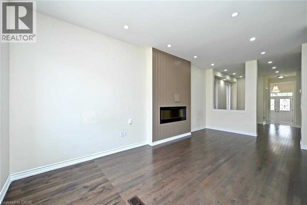 Wide plank wood-finish flooring, recessed lighting, contemporary fireplace with a fluted surround, half wall with a decorative niche, and double entry doors - 64 Maple Cider Street, Caledon, ON