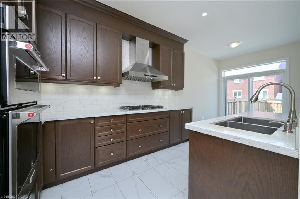 Kitchen featuring dark wood-finish cabinetry, light-toned countertops, white subway tile backsplash, stainless steel appliances, and a double basin sink with a gooseneck faucet - 64 Maple Cider Street, Caledon, ON