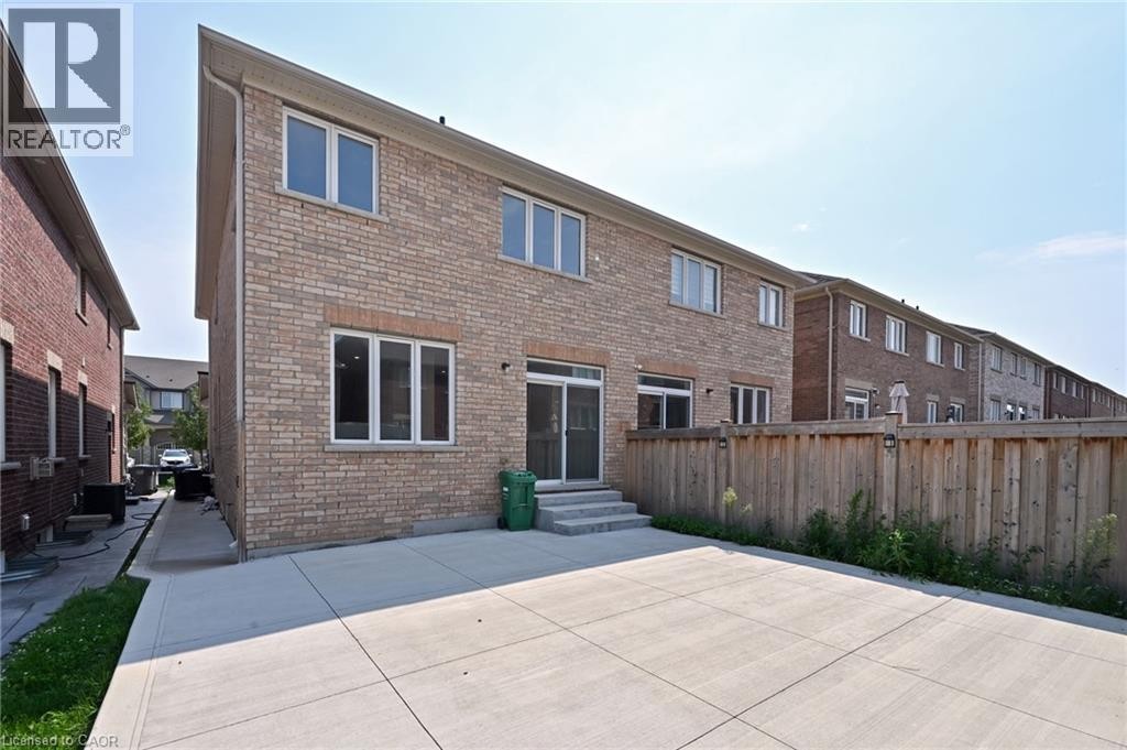 Brick exterior with multiple windows, concrete patio, and a wood fence - 64 Maple Cider Street, Caledon, ON