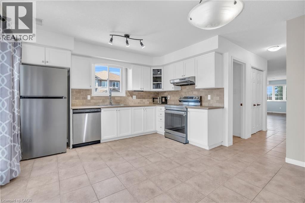 Kitchen featuring white cabinetry, stainless steel appliances, neutral tile flooring, tile backsplash, and track lighting - 50 Howe Drive Unit# 19B, Kitchener, ON