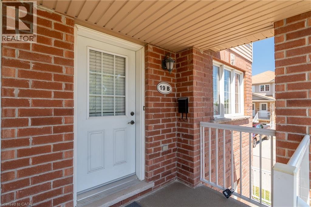 Red brick exterior with white trim, white entry door with louvered glass, exterior wall-mounted lighting, and a white railing - 50 Howe Drive Unit# 19B, Kitchener, ON