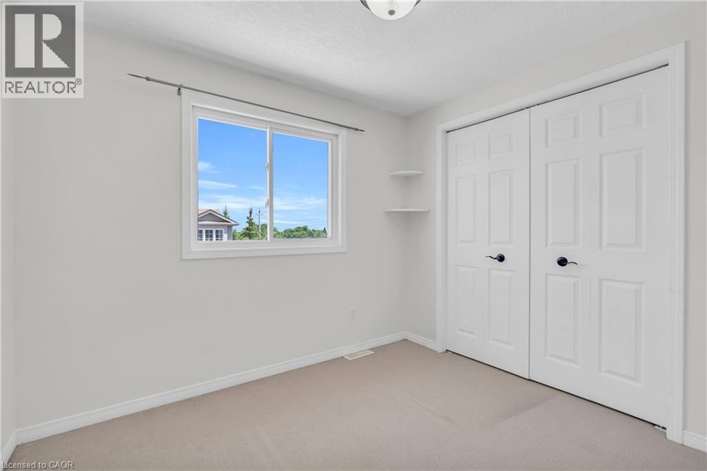 Neutral wall color, carpeted flooring, sliding window with white trim, built-in shelving, and bifold closet doors - 50 Howe Drive Unit# 19B, Kitchener, ON