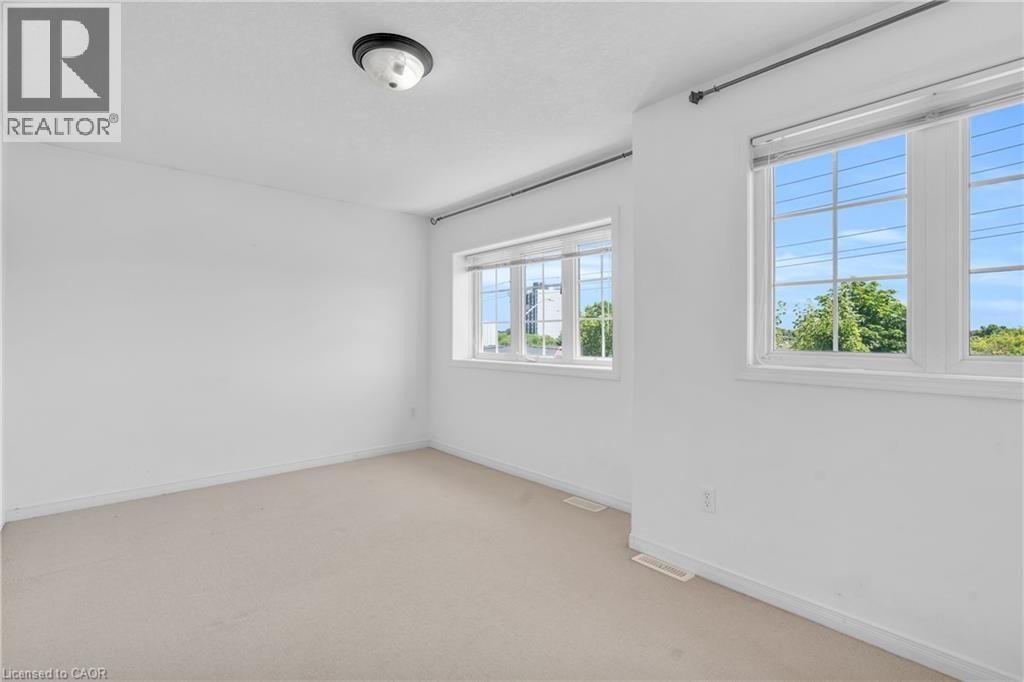 Neutral carpeted flooring, white painted walls, and multiple windows with grids - 50 Howe Drive Unit# 19B, Kitchener, ON