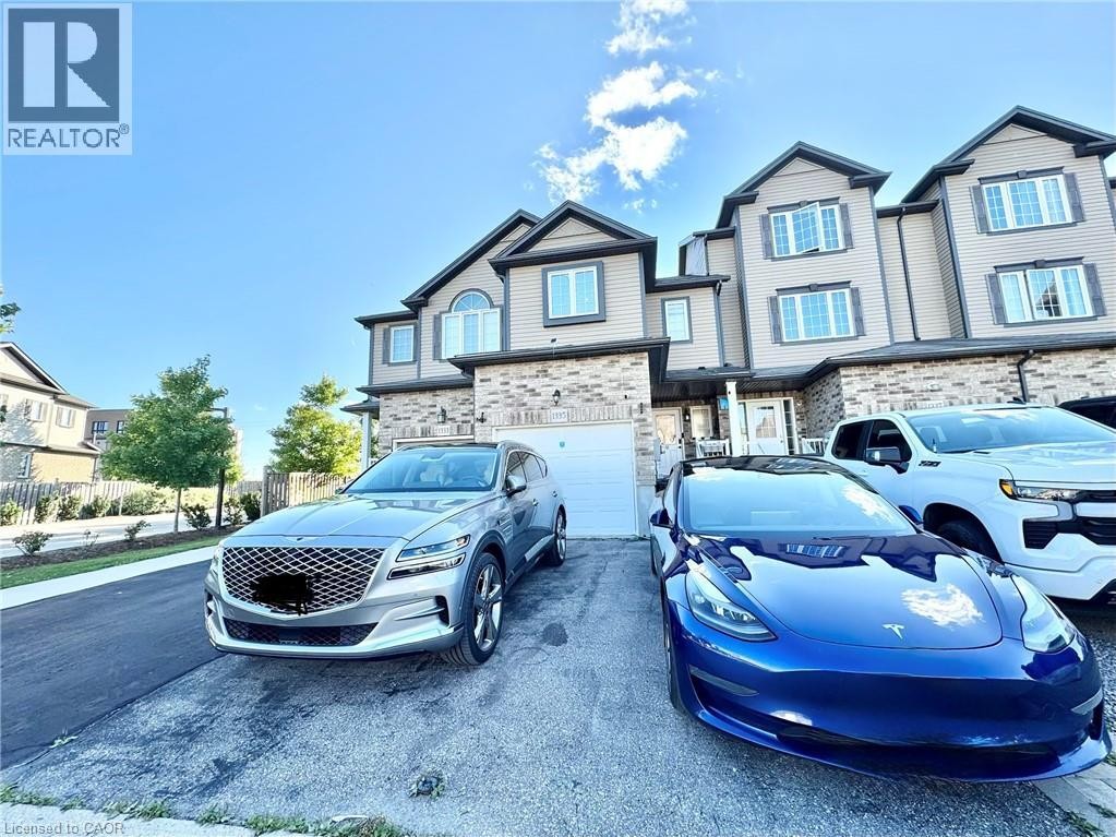 Modern townhome exterior featuring light-toned siding, brick accents, multiple windows, and an attached garage - 1335 Countrystone Drive, Kitchener, ON