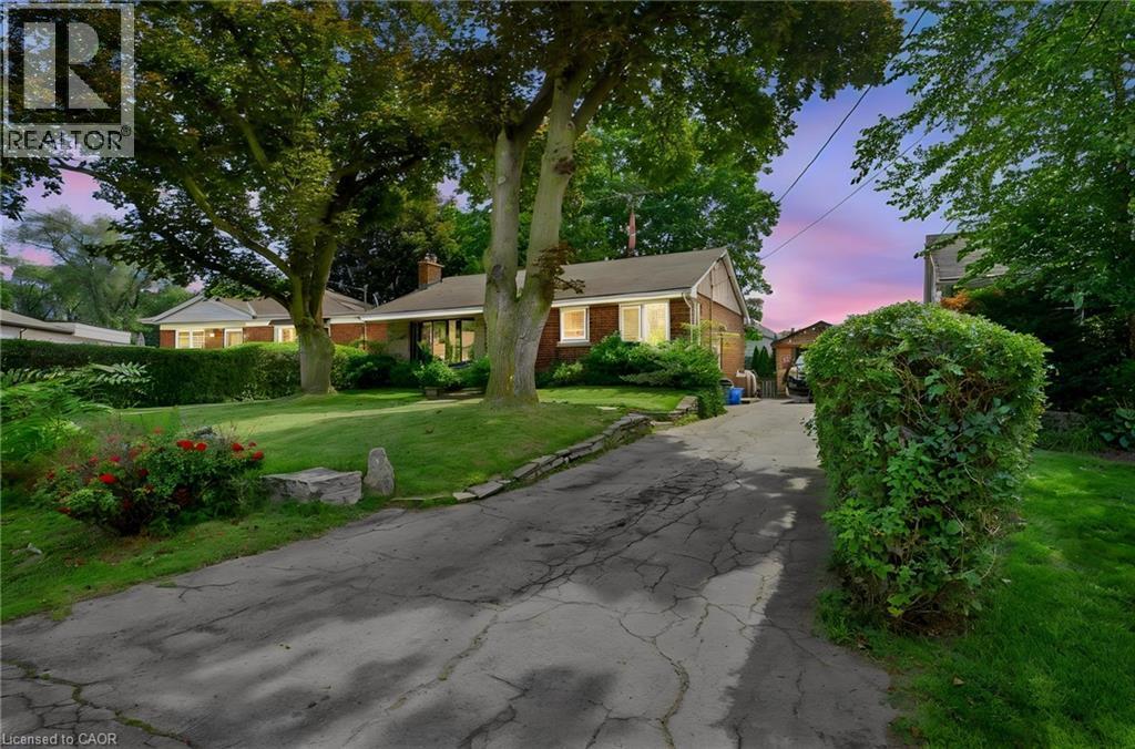 Brick exterior residence with a sloped driveway, mature trees, and landscaping - 1046 Shepherds Drive, Burlington, ON