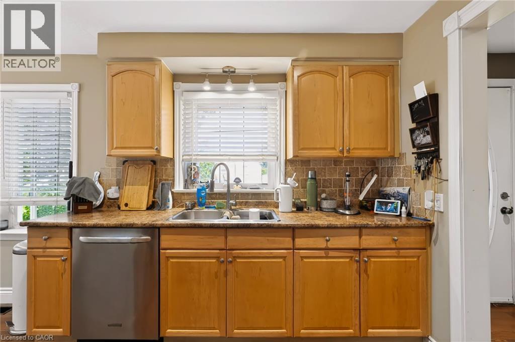 Wood-finish cabinetry, stainless steel dishwasher, tile backsplash, dual basin stainless steel sink, and light-tone countertops - 1046 Shepherds Drive, Burlington, ON