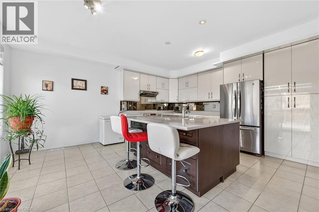 Kitchen with a breakfast bar, freestanding refrigerator, dual tone cabinets, a center island with sink, and light tile patterned flooring - 97 Sirente Drive, Hamilton, ON