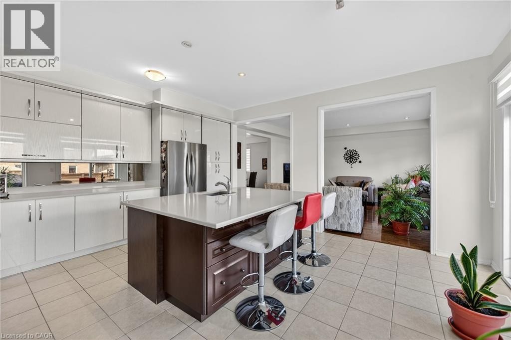 Dual tone kitchen with dual tone cabinetry, freestanding refrigerator, a kitchen bar, an island with sink, and light tile patterned floors - 97 Sirente Drive, Hamilton, ON