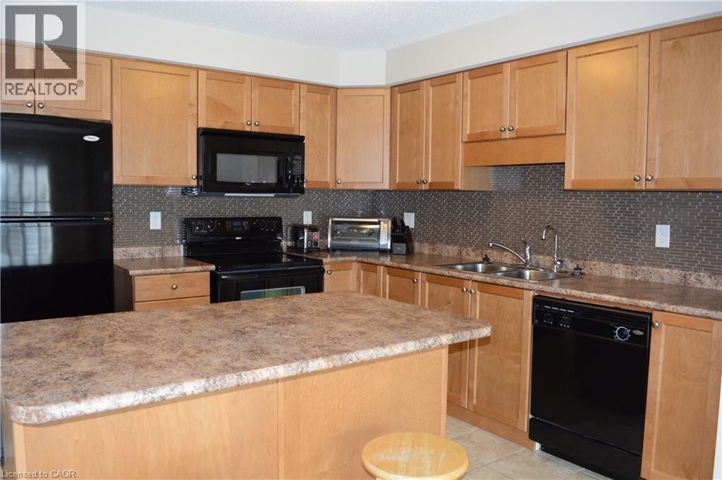 Kitchen featuring natural wood-finish cabinetry, black appliances, a central island, and a mosaic tile backsplash - 507 Beaumont Crescent, Kitchener, ON