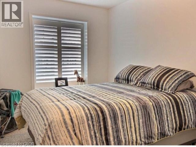 Bright bedroom showcasing neutral striped bedding, plantation shutters with adjustable louvers, and carpeted flooring - 507 Beaumont Crescent, Kitchener, ON