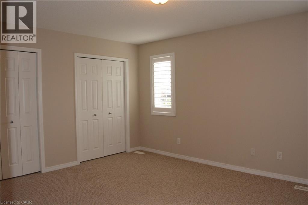 Neutral paint palette with textured carpeting, two bi-fold door closets, and a window featuring white plantation shutters - 507 Beaumont Crescent, Kitchener, ON