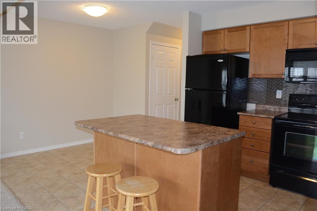Open kitchen featuring wood-finish cabinetry, granite-style countertops, a large island with seating, stainless steel appliances, and tile flooring throughout the living and dining areas - 507 Beaumont Crescent, Kitchener, ON