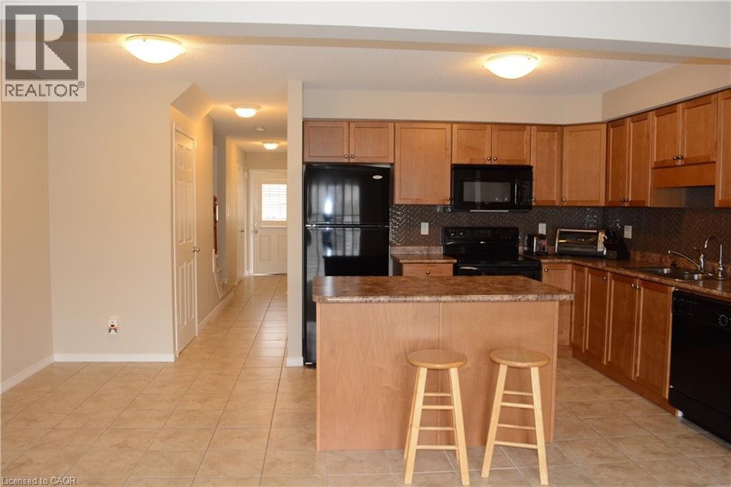 Kitchen featuring wood cabinetry, an island with countertop, black appliances, and a tiled backsplash - 507 Beaumont Crescent, Kitchener, ON