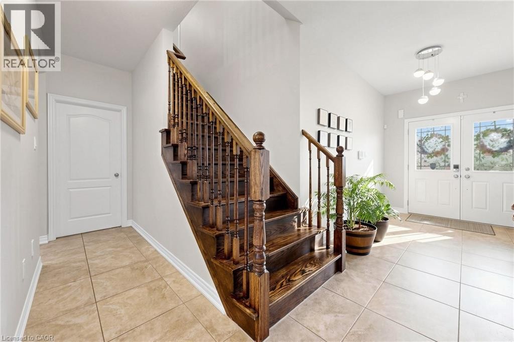 Hardwood staircase with turned spindles, tile flooring, white interior doors, and double entry doors with decorative glass inserts - 173 Raymond Road, Ancaster, ON