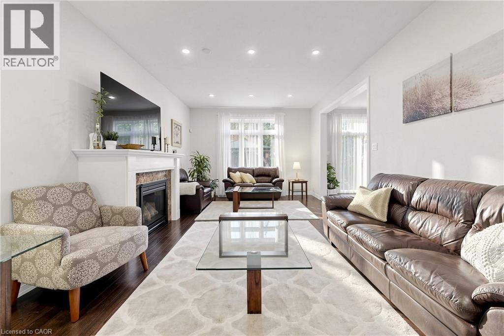 Bright living area with wood-finish flooring, recessed lighting, a fireplace with a stone surround and mantel, and white window coverings - 173 Raymond Road, Ancaster, ON