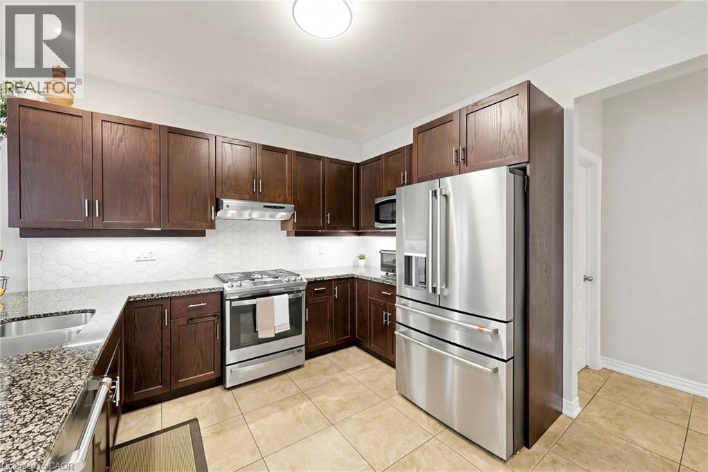 Stainless steel appliance suite, dark wood cabinetry, light tile flooring, hexagonal tile backsplash, and stone countertops - 173 Raymond Road, Ancaster, ON