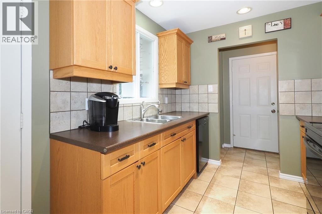 Kitchen featuring light wood cabinetry, a dual-basin sink, tile backsplash, laminate countertops, and tile flooring - 219 Foxhunt Road, Waterloo, ON