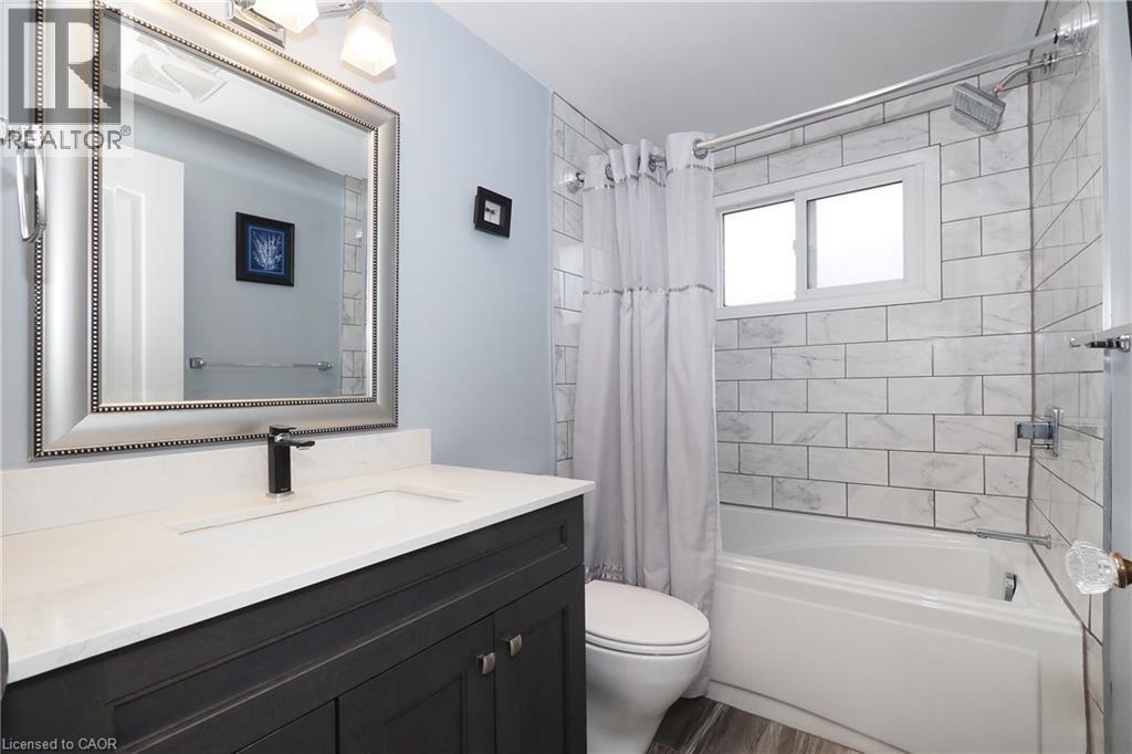 Vanity with a white countertop and dark cabinetry, wood-finish flooring, white subway tile shower surround, and a built-in bathtub - 219 Foxhunt Road, Waterloo, ON