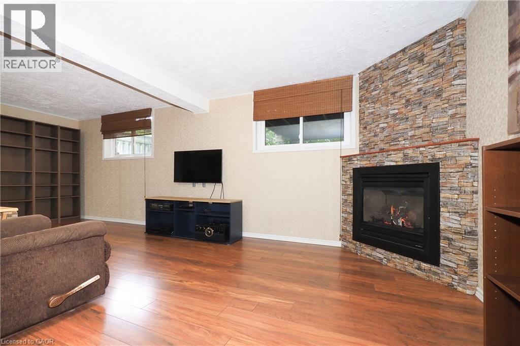 Wood-finish flooring, built-in shelving, windows with blinds, and a corner fireplace with a stone surround - 219 Foxhunt Road, Waterloo, ON