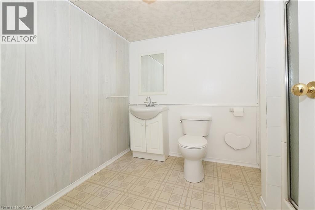 White wood-finish paneling, white vanity with integrated sink, toilet, wall-mounted mirror, and tiled flooring - 219 Foxhunt Road, Waterloo, ON