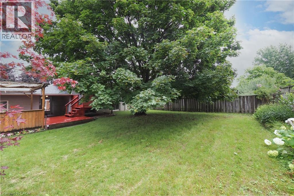 Expansive backyard with a manicured lawn, mature trees, and a wooden privacy fence - 219 Foxhunt Road, Waterloo, ON