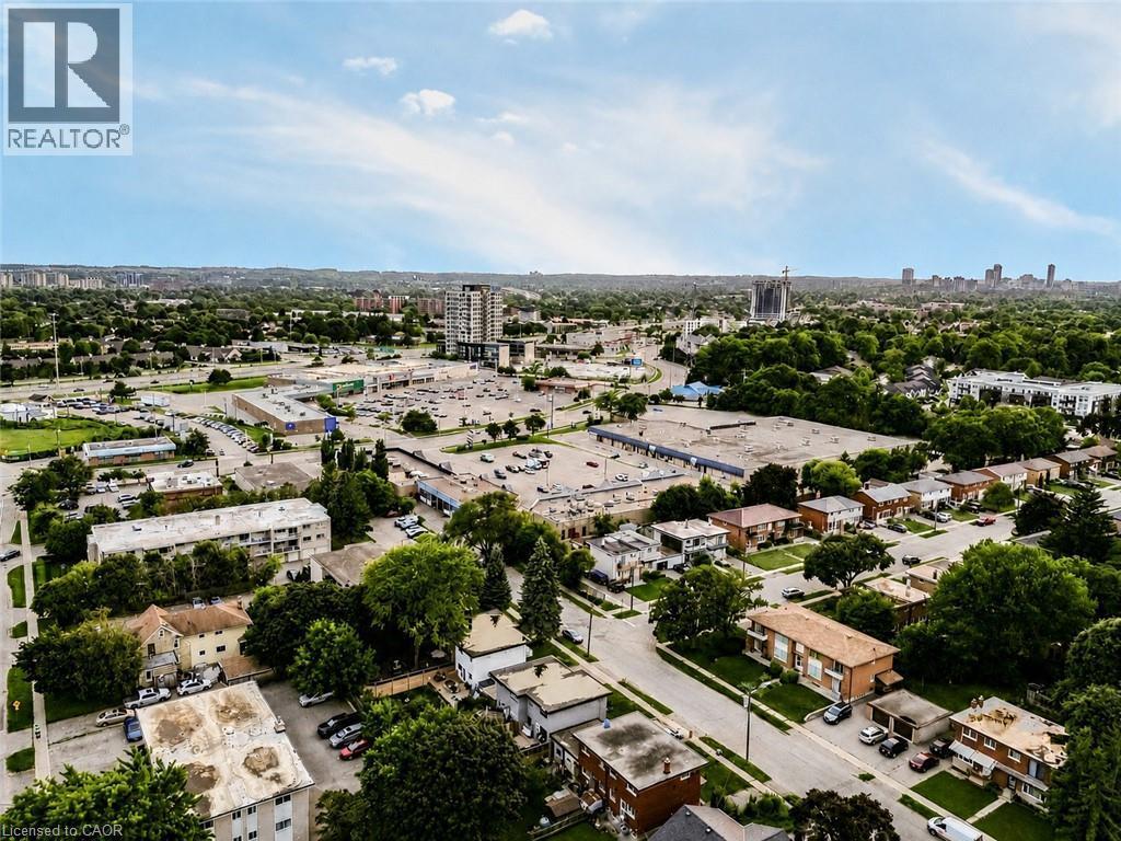 Aerial perspective showcasing a residential neighborhood with mature trees, commercial establishments, and a distant urban skyline - 67 Kinzie Avenue, Kitchener, ON