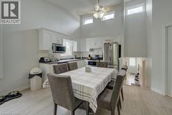 Open-concept kitchen and dining area featuring vaulted ceilings with high windows, white cabinetry, dark countertops, stainless steel appliances, and light wood-finish flooring - 