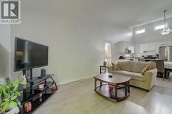 Open-concept living space featuring wood-finish flooring, vaulted ceilings, and upper transom windows - 