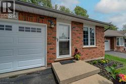 Red brick exterior featuring a white garage door with upper window inserts, white-framed windows, a concrete walkway, and a landscaped garden bed - 