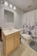 Bathroom featuring a light wood-finish vanity with a single sink and light-toned countertop, a wall-mounted mirror, and a three-light vanity fixture - 