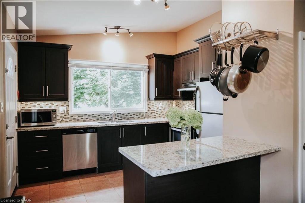 Kitchen featuring dark wood cabinetry, light-toned countertops, a mosaic tile backsplash, stainless steel appliances, and a window above the sink - 1 Vera Court, Hamilton, ON