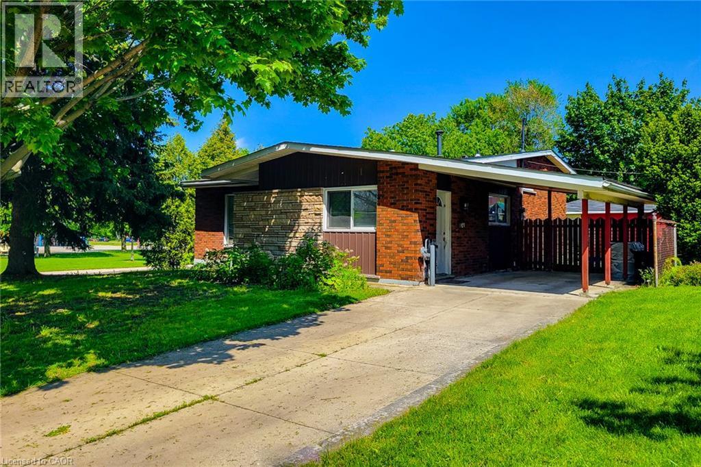 Brick and stone facade with a covered carport, mature trees, and a wooden privacy fence - 1 Vera Court, Hamilton, ON