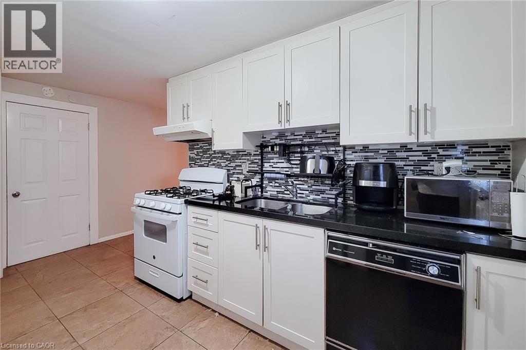 Kitchen featuring white cabinetry, black countertops, a mosaic tile backsplash, and tile flooring - 1 Vera Court, Hamilton, ON
