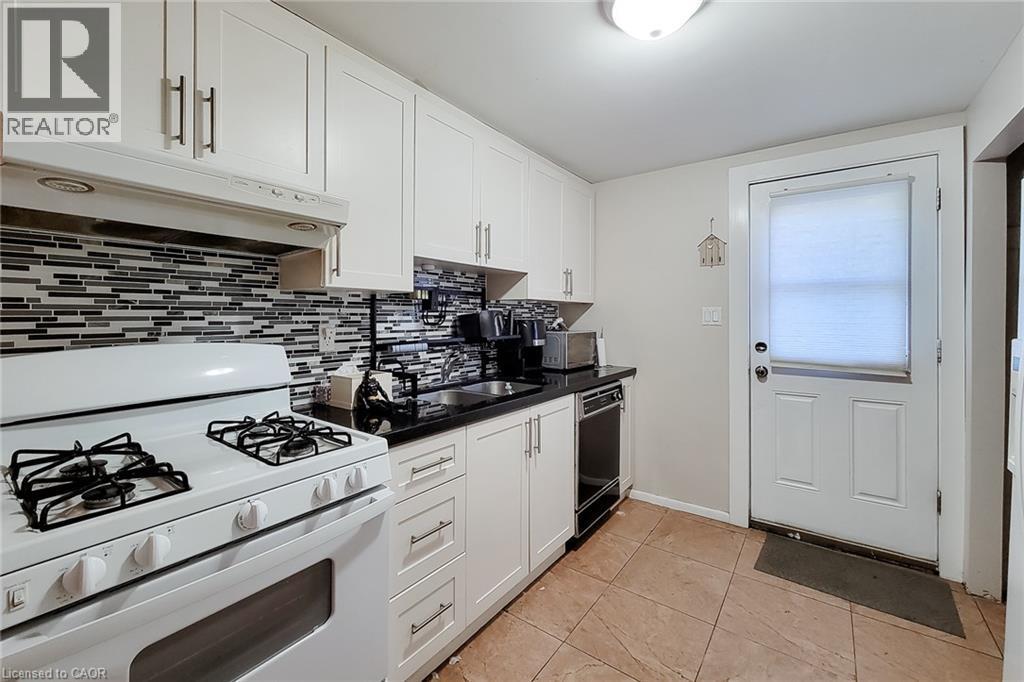 White cabinetry with brushed nickel hardware, black countertop, mosaic tile backsplash, and white range - 1 Vera Court, Hamilton, ON