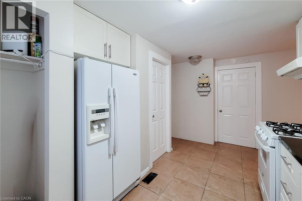 White kitchen cabinetry with brushed nickel hardware, side-by-side refrigerator, tile flooring, and white paneled doors - 1 Vera Court, Hamilton, ON