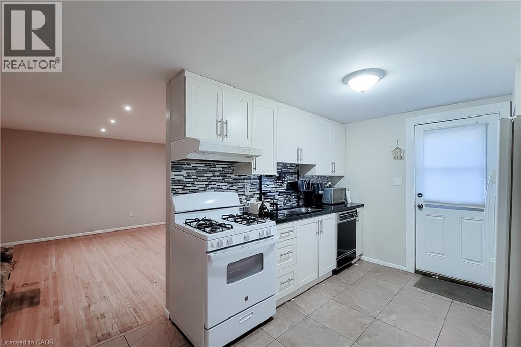 Kitchen featuring white cabinetry, a mosaic tile backsplash, black countertops, and a full-size range - 1 Vera Court, Hamilton, ON