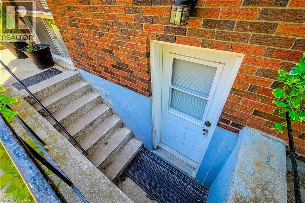 Brick exterior with a white entry door, concrete steps, and a black handrail - 1 Vera Court, Hamilton, ON