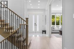 Foyer featuring a light wood-finish staircase with contemporary black metal balusters, polished tile flooring, and a double entry door with frosted glass panels - 