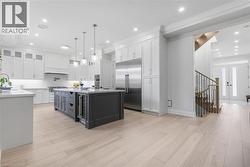 Contemporary kitchen featuring white cabinetry, a dark-toned island with integrated beverage refrigerator, stainless steel appliances, and light wood-finish flooring - 