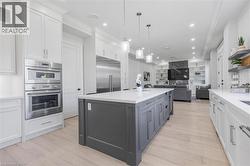 Gourmet kitchen featuring a large island with gray cabinetry and white countertops, integrated stainless steel appliances including a built-in oven and microwave, light wood-finish flooring, and reces - 